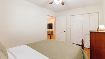 A bedroom with a bed, a ceiling fan, a dresser, and a door leading to another room.