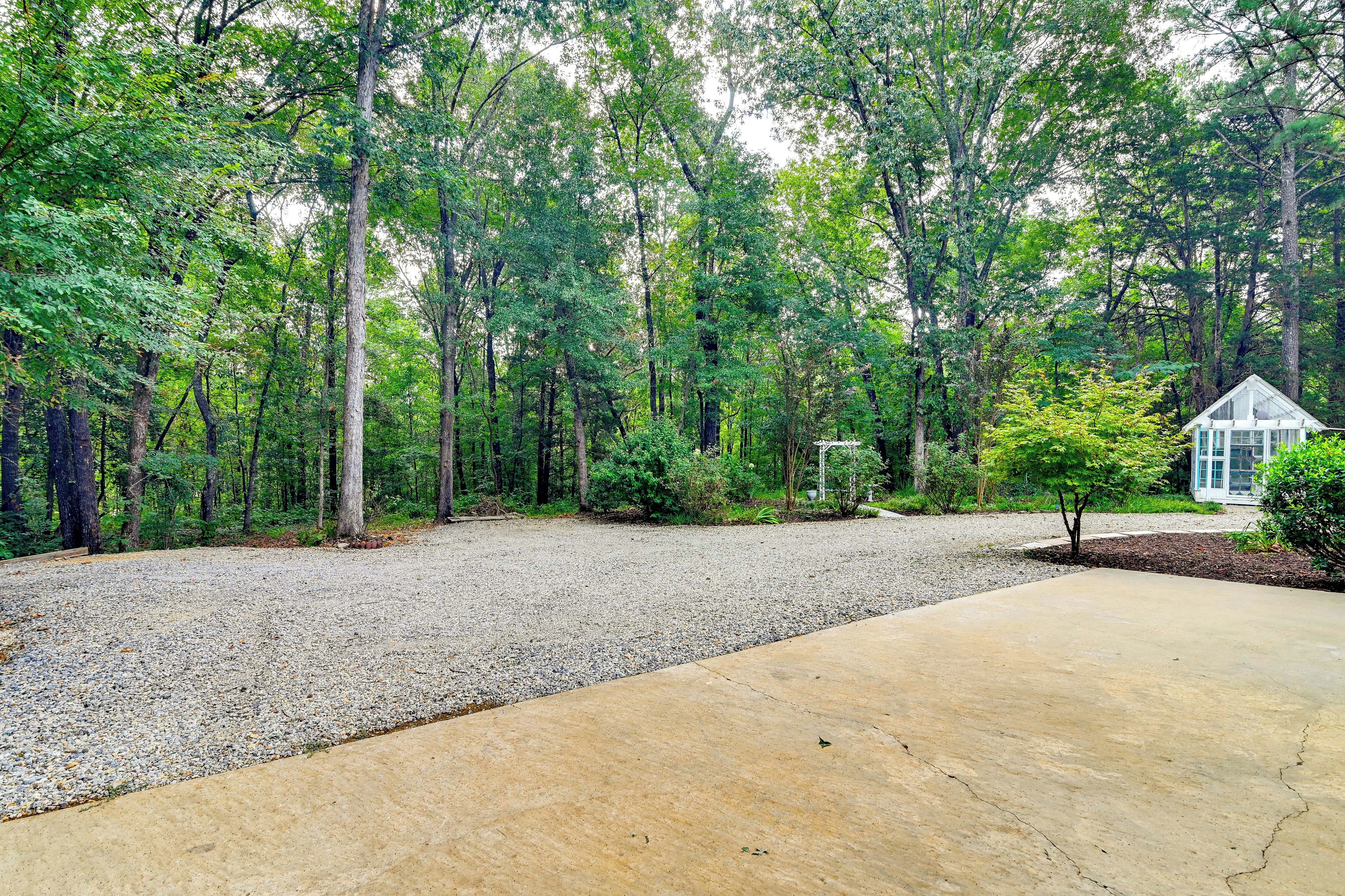 A gravel driveway leading to a house with a small garden area, surrounded by a dense forest.