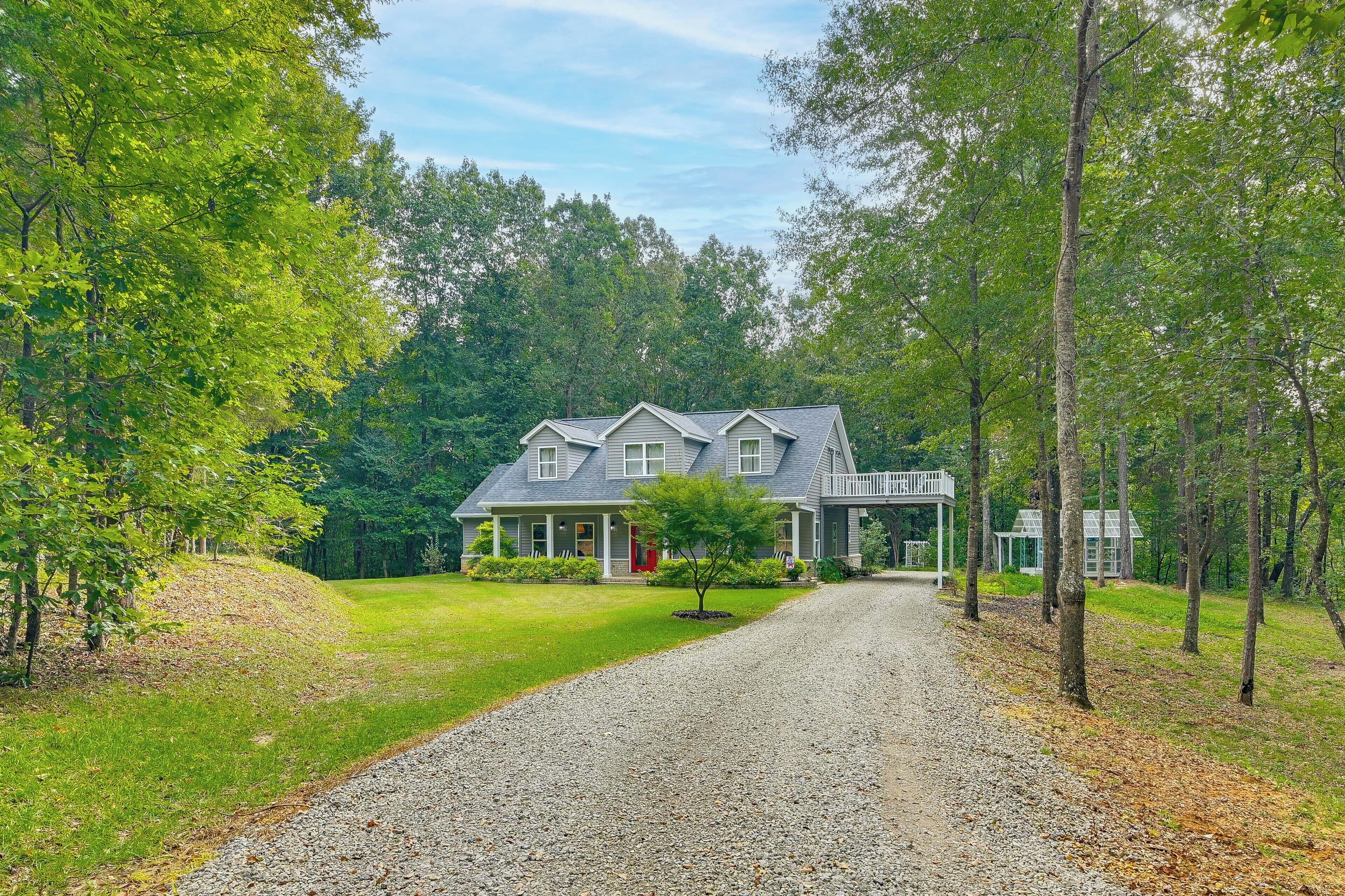 A two-story house with a covered porch and a gravel driveway leading to the entrance.