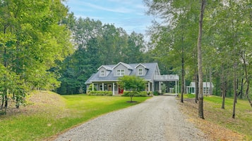 A two-story house with a covered porch and a gravel driveway leading to the entrance.