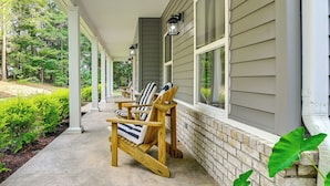 A covered porch with wooden chairs and a table, a brick wall, and a window. - Private Woodland Garden Retreat in Ethelsville (Ethelsville)