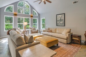 Ein geräumiges Wohnzimmer mit hoher Decke, großen Fenstern und Deckenventilator.