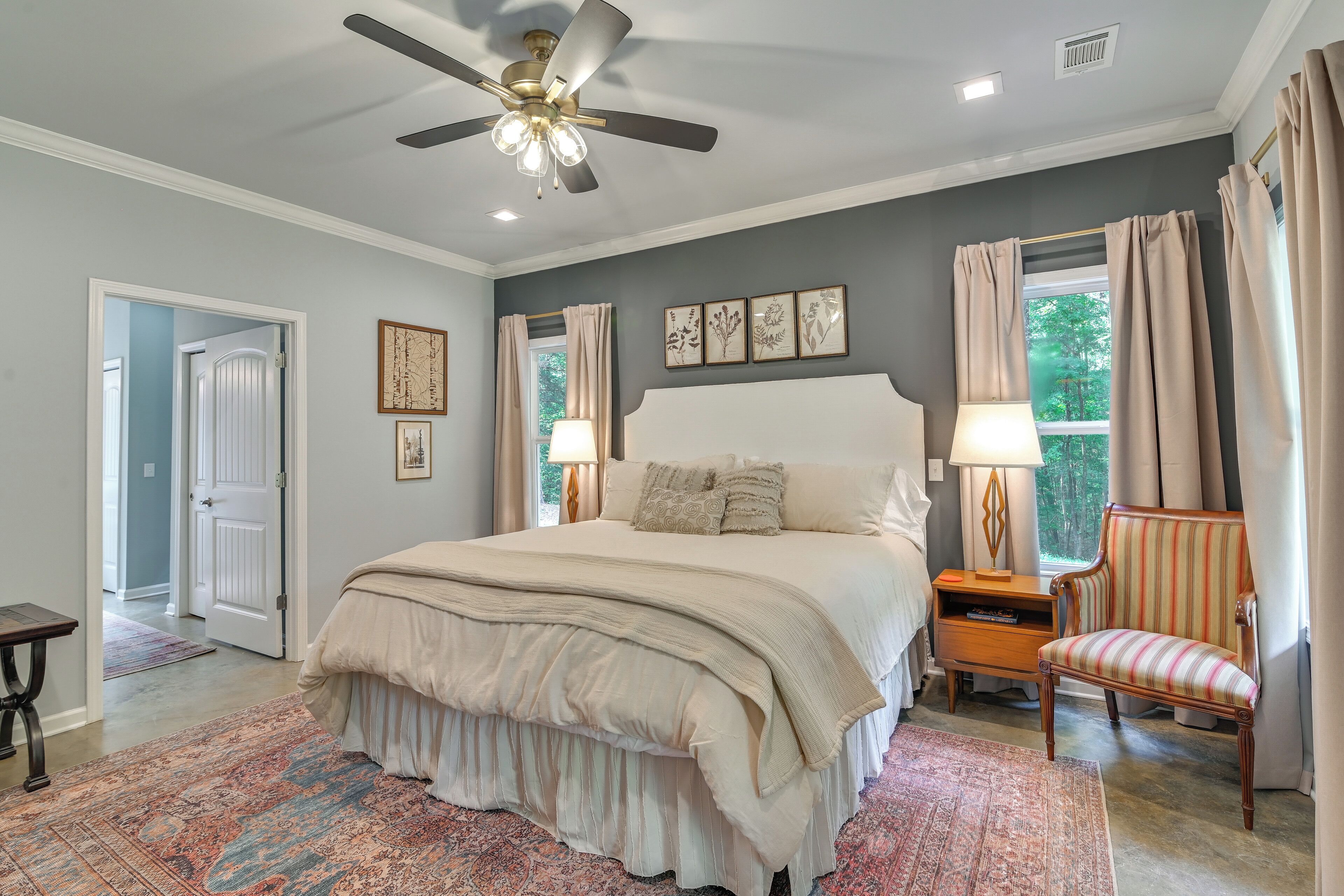 A bedroom with a bed, a chair, a nightstand, a ceiling fan, and a window with curtains.