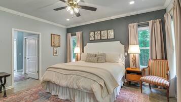 A bedroom with a bed, a chair, a nightstand, a ceiling fan, and a window with curtains.