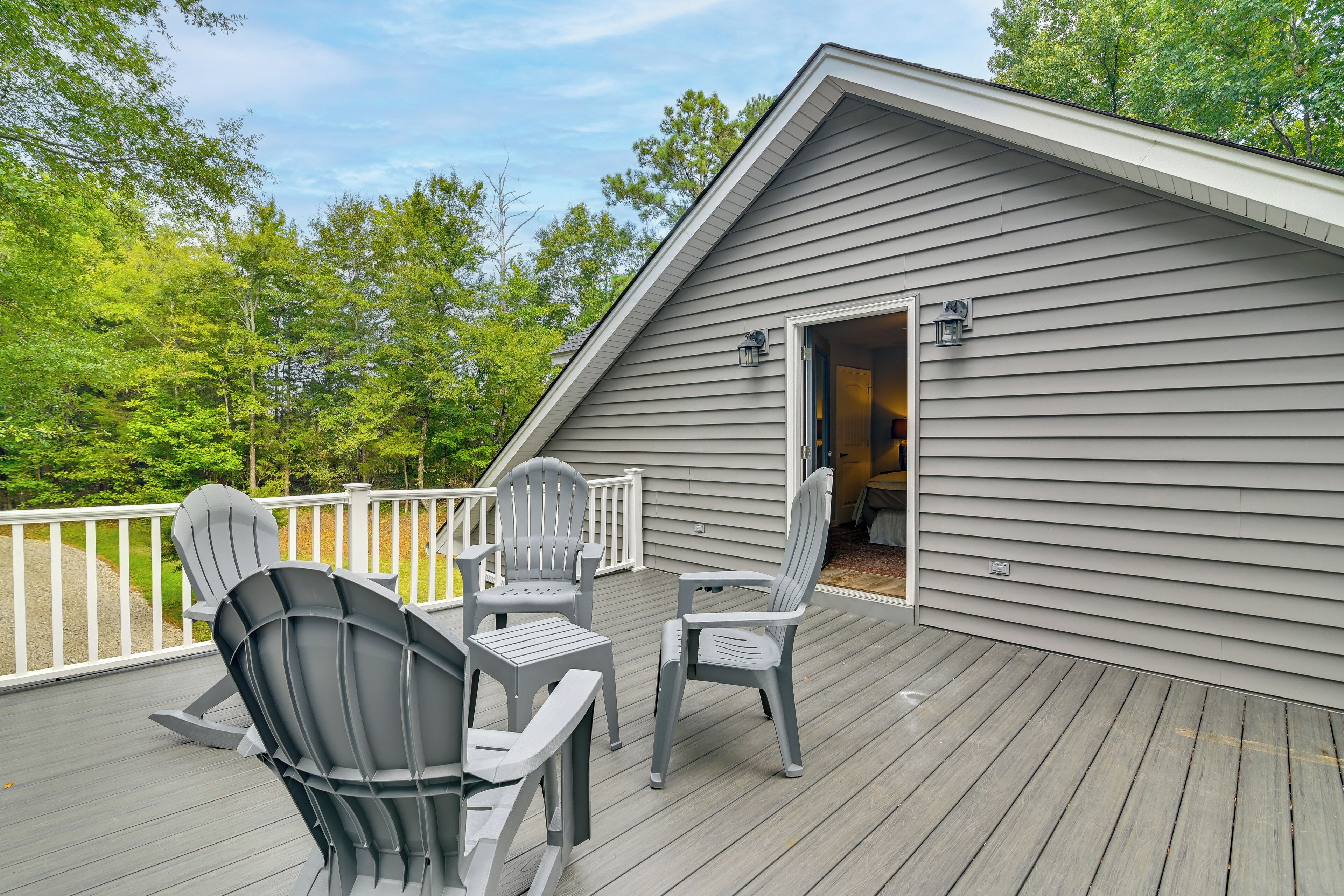 A deck with Adirondack chairs and a small table, a wooden deck, and a building with a door leading to an interior space.