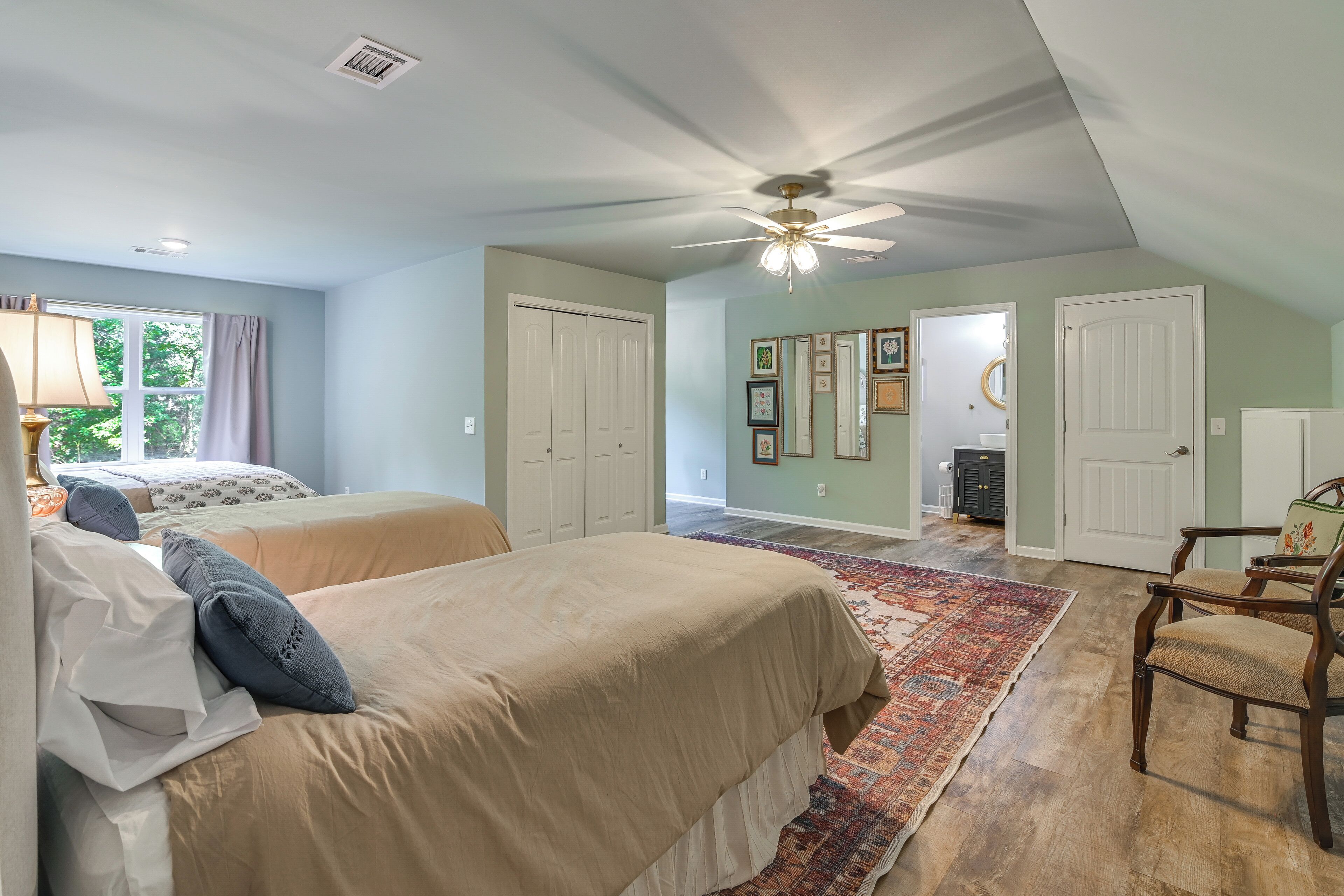 A bedroom with two beds, a ceiling fan, a window with curtains, and a door leading to another room.