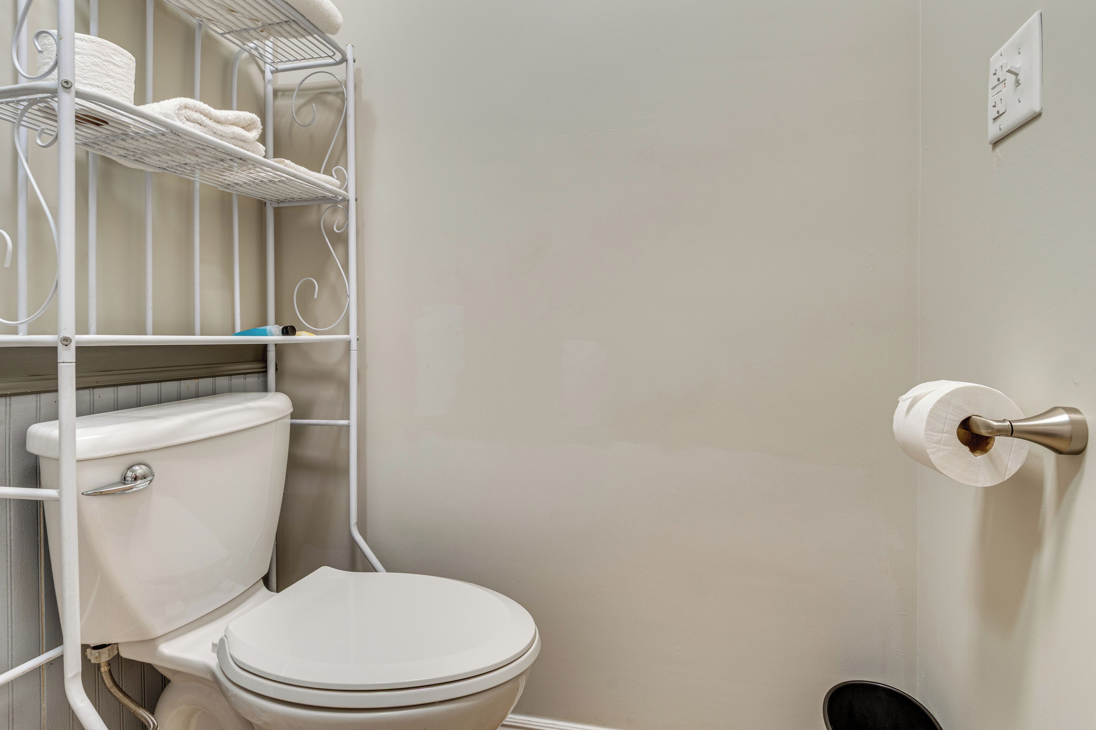 A bathroom with a toilet, a shelf with towels, and a toilet paper holder.