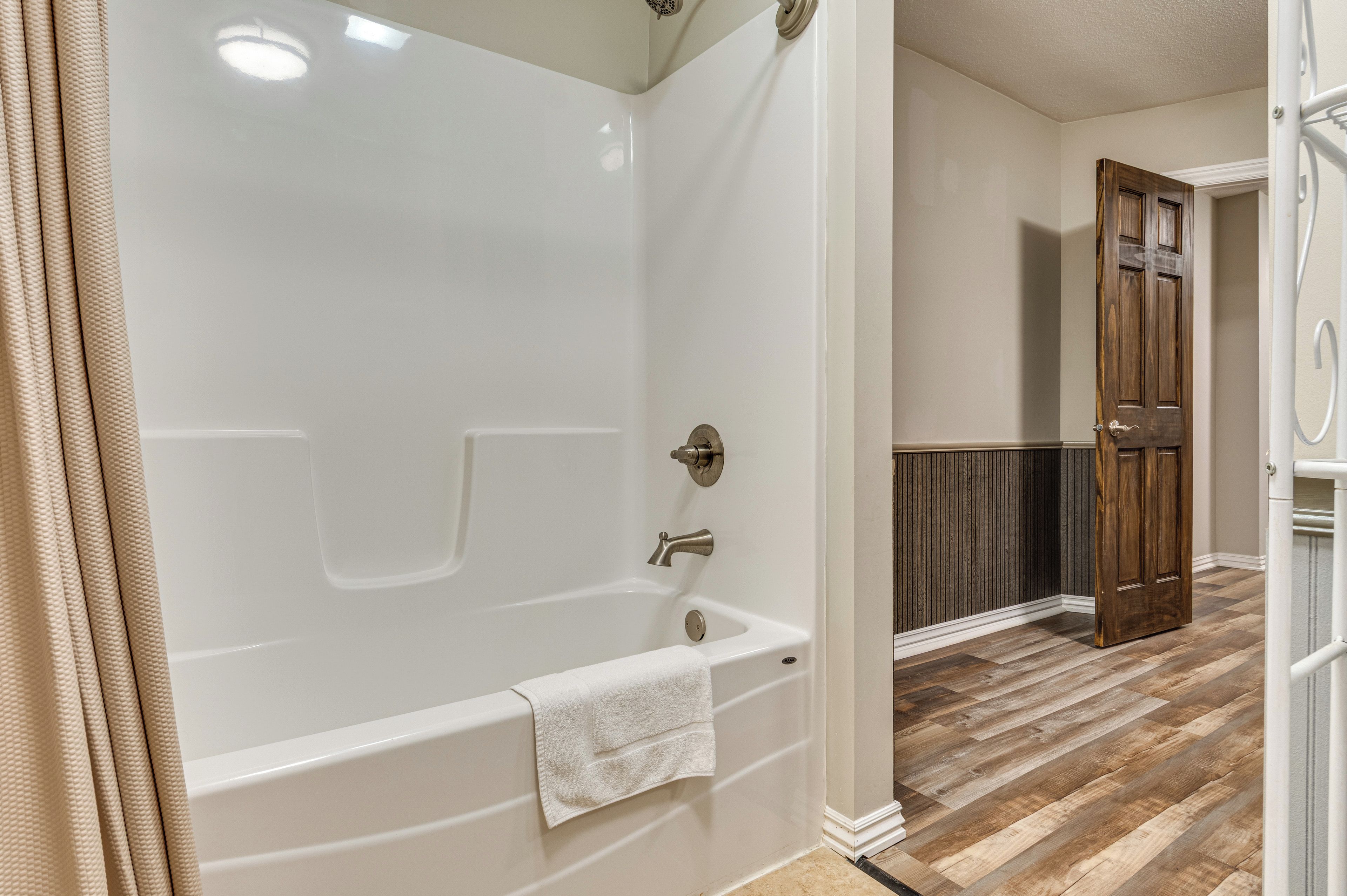 Un baño con bañera, toalla y puerta de madera.