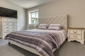 Un dormitorio con cama, cómoda, televisor y ventana.