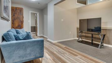 A modern living room with a blue sofa, a wooden floor, a TV on a stand, and a door leading to another room.