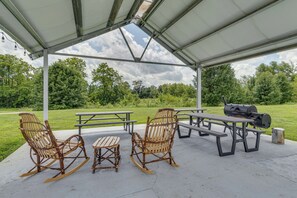An outdoor covered picnic area with picnic tables, chairs, and a grill.