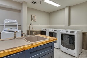 A laundry room with a sink, two washing machines, and a wooden countertop.