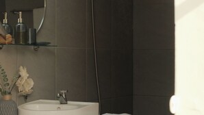 Un baño con un lavamanos blanco, un espejo, una toalla con el bordado 'Kalipayon' y un cabezal de ducha.