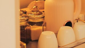 Una cafetera con un preparador de goteo, una bandeja con tazas y un recipiente para azúcar.