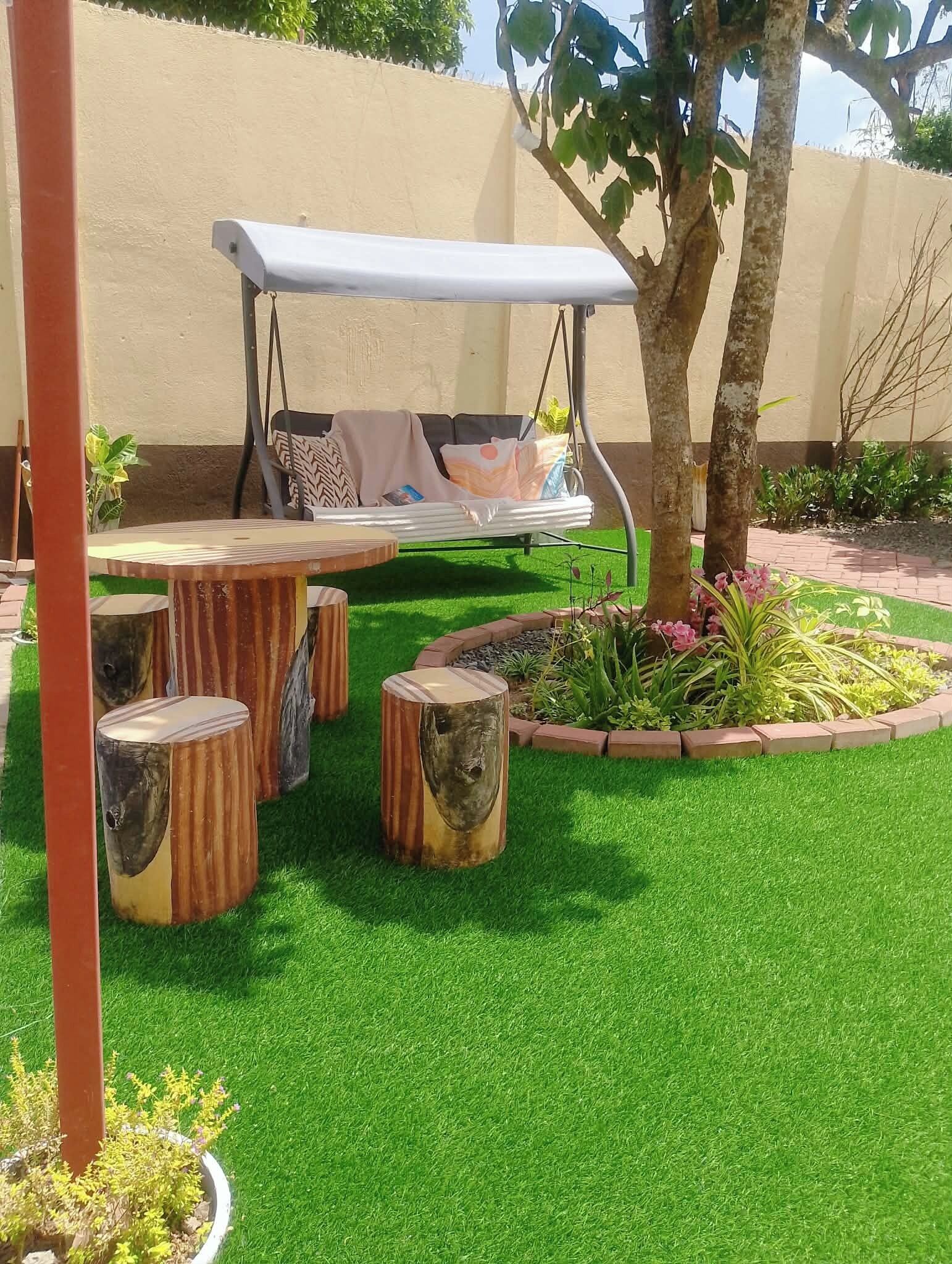 Un jardín con un columpio, taburetes de madera y un césped bien cuidado.