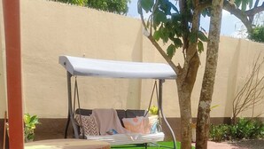 Un jardín con un columpio, taburetes de madera y un césped bien cuidado.