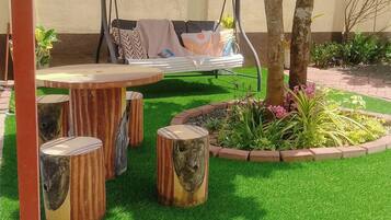 Un jardín con un columpio, taburetes de madera y un césped bien cuidado.