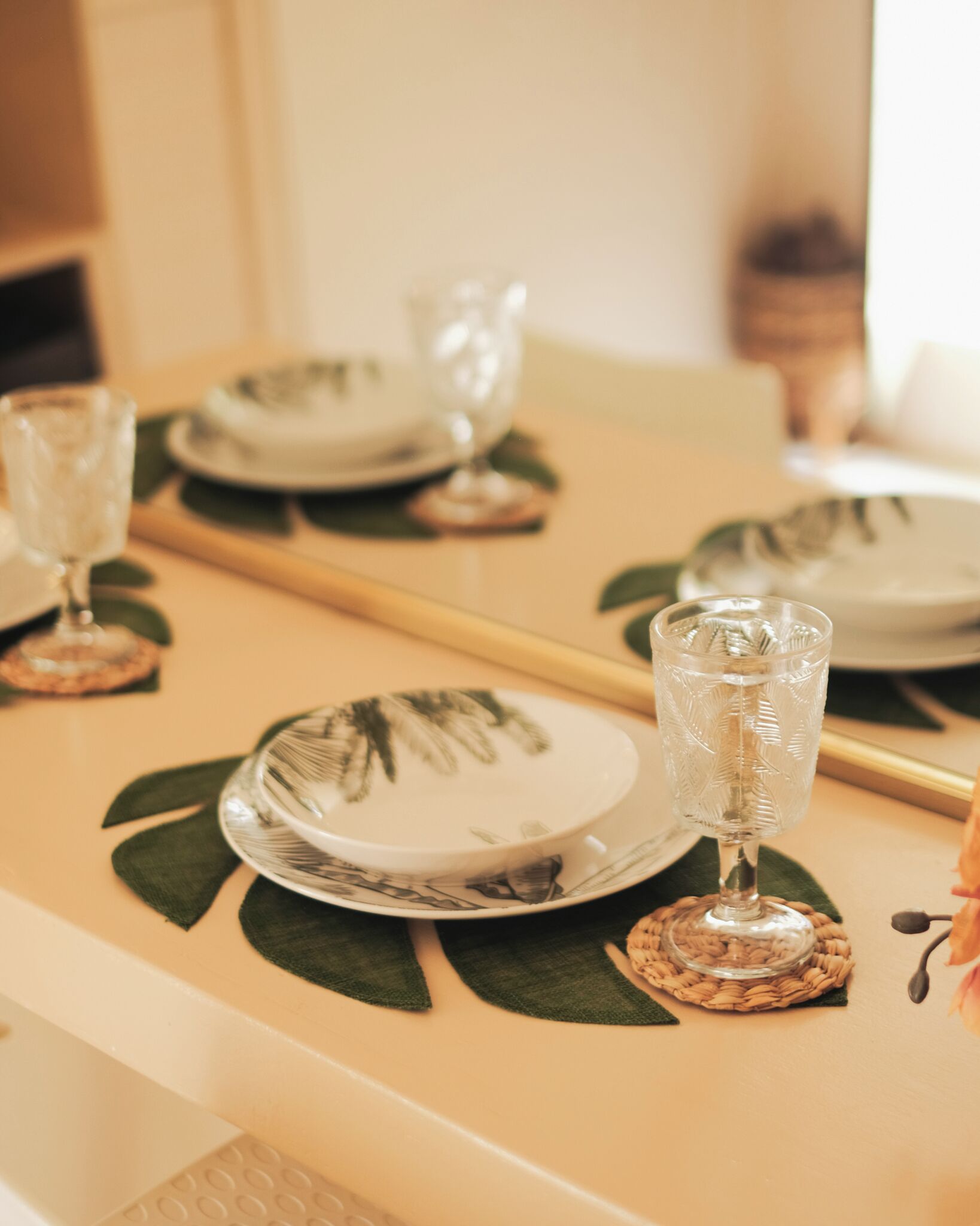 Une table à manger dressée avec des assiettes, des verres et un set de table décoratif en forme de feuille.