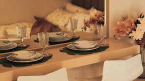 Un área de comedor con una mesa lista para dos personas, dos sillas y un florero con flores.