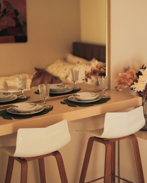 Un área de comedor con una mesa lista para dos personas, dos sillas y un florero con flores.