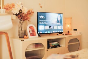 Un televisor sobre un atril de madera, un jarrón con flores y un cuadro enmarco.