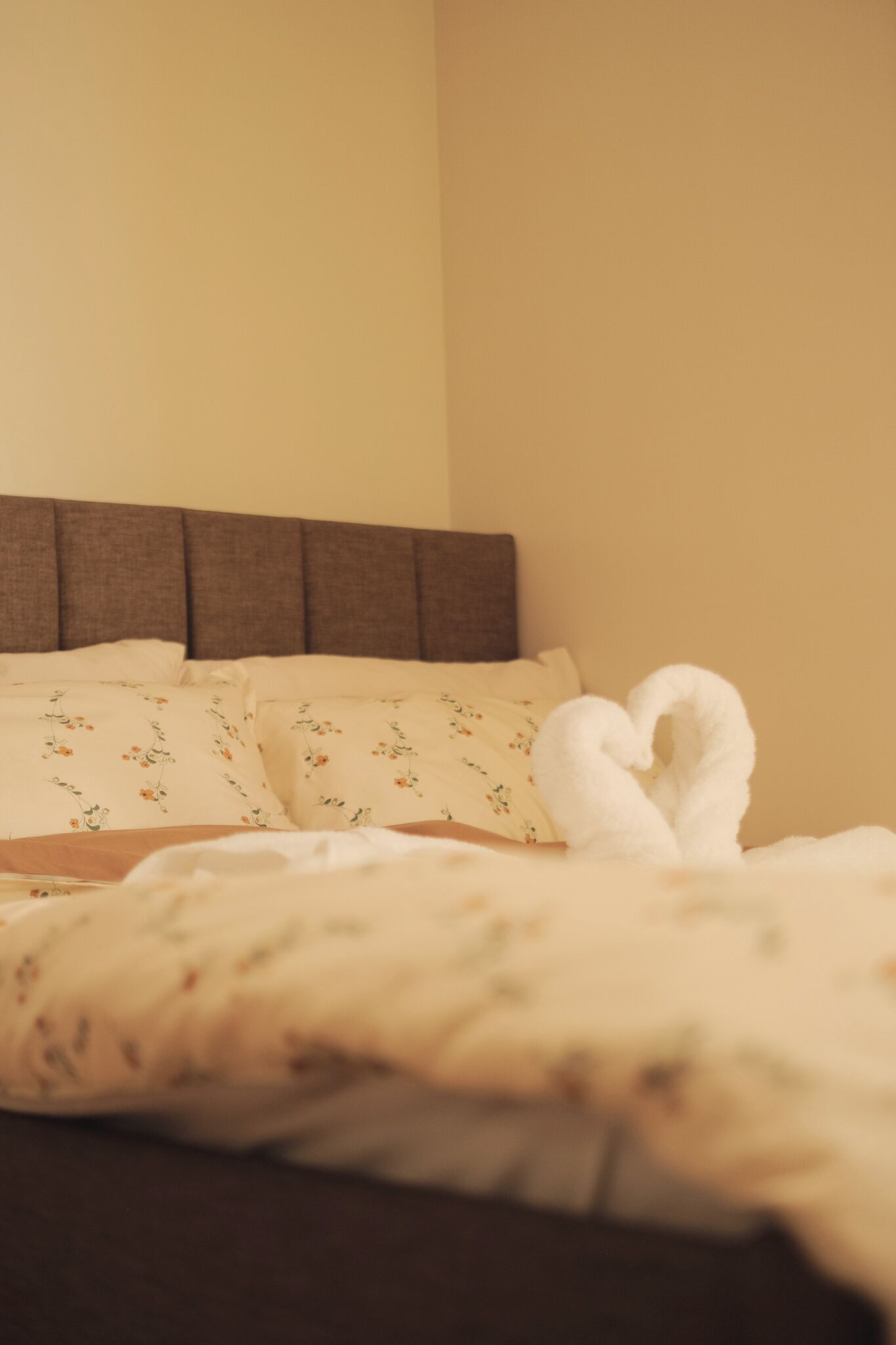 A bed with a heart-shaped towel and floral-patterned pillows.