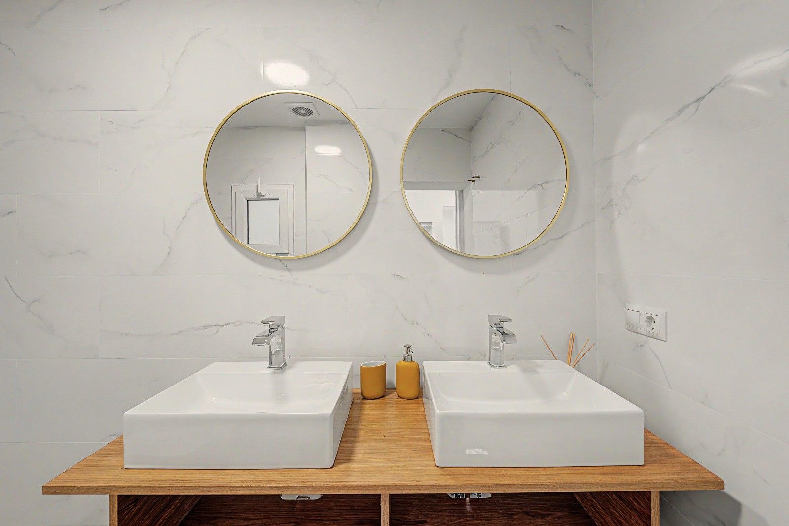 A bathroom with two sinks, each with a modern faucet, and two round mirrors with gold frames.