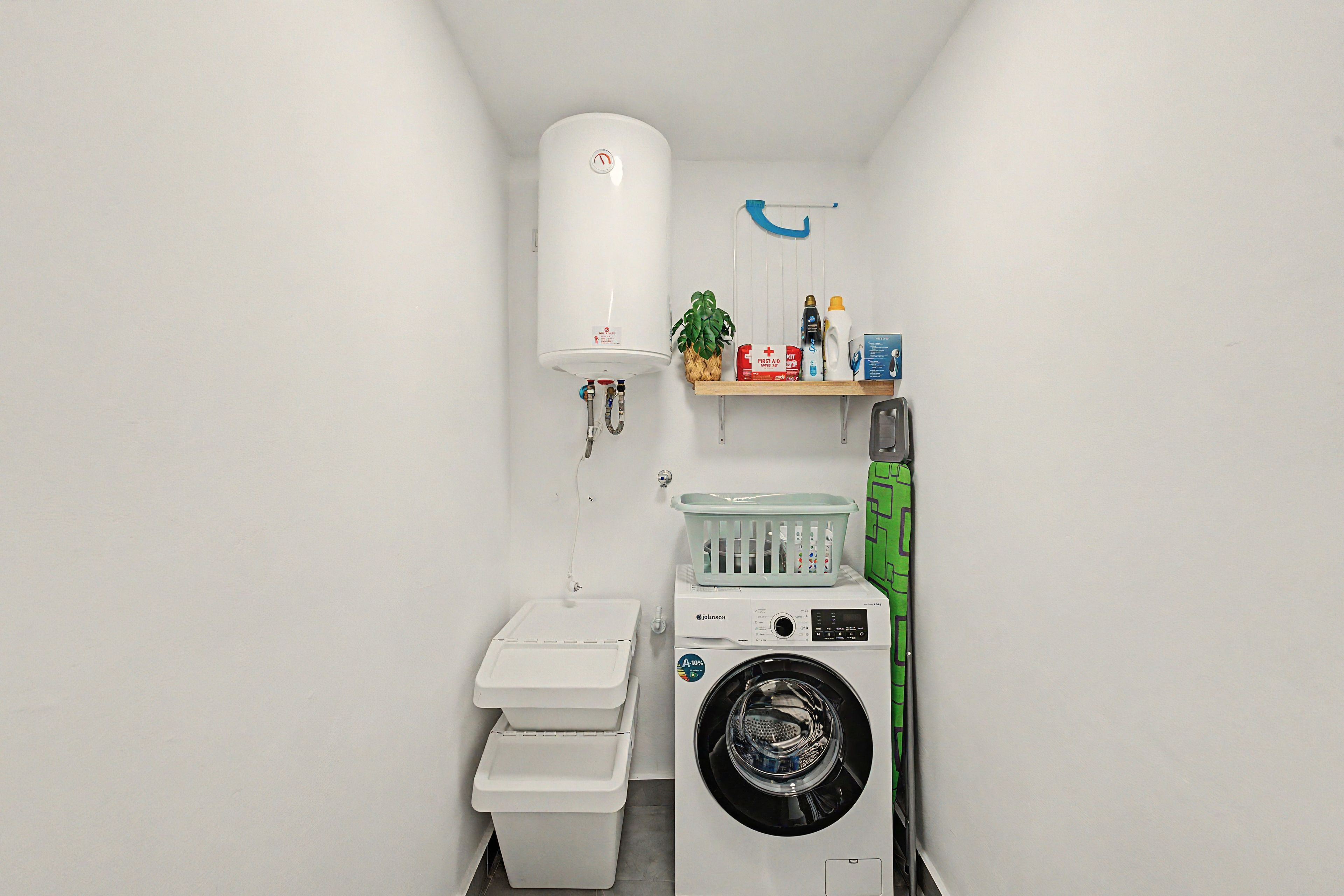 A compact bathroom with a toilet, washing machine, and a shelf with toiletries.