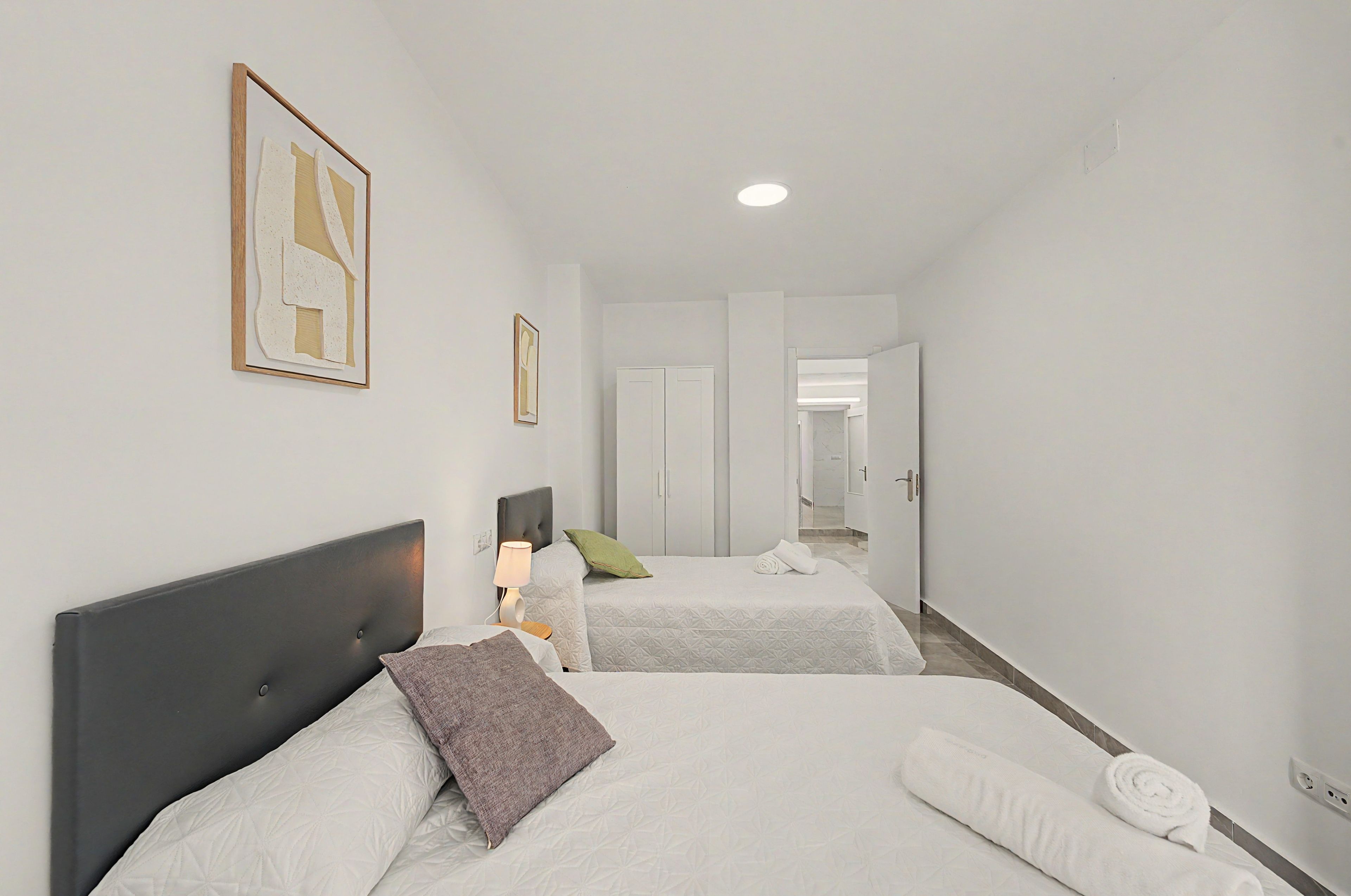 Een hotelkamer met twee bedden, een nachtkastje met een lamp, en een gang naar een badkamer.