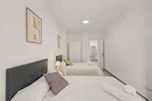 Hotellihuone, jossa on kaksi sänkyä, yöpöytä lampun kanssa ja käytävä, joka johtaa kylpyhuoneeseen.