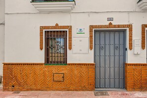 Fachada de edificio con puerta metálica, ventana con celosías decorativas y un cartel con dirección rural.