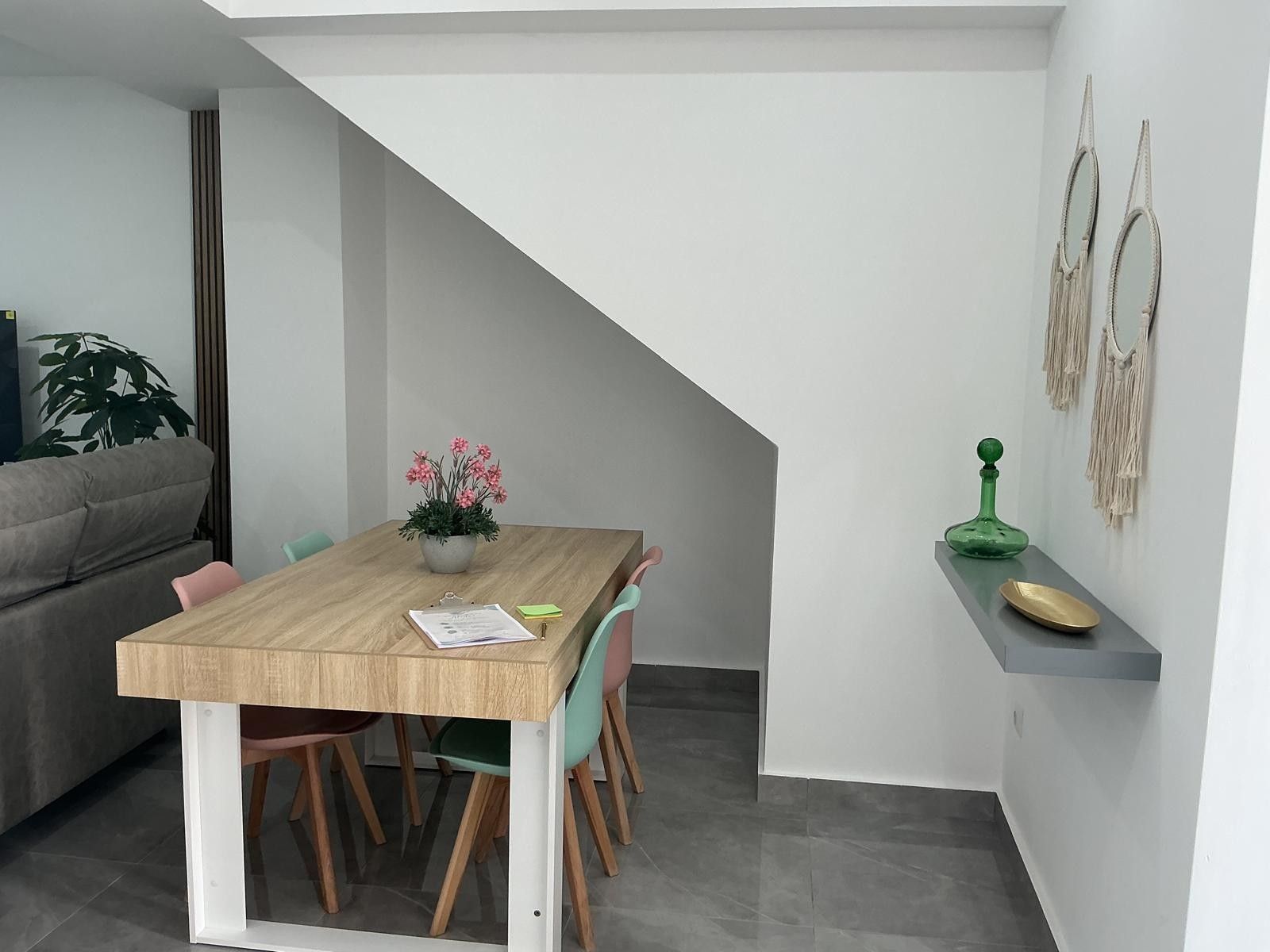 Un comedor con una mesa de madera, sillas, una planta en maceta y una botella verde en un estante.