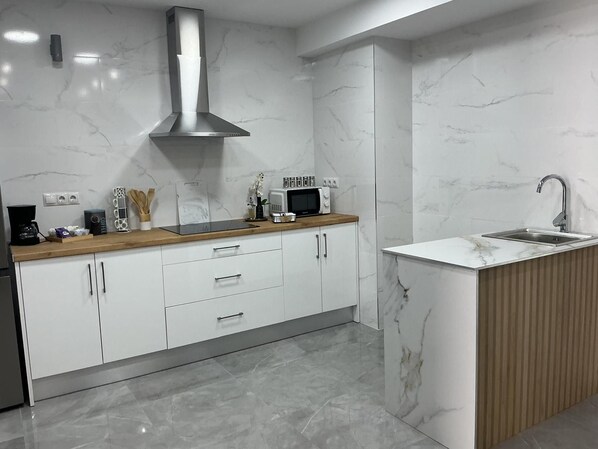 A modern kitchen with white cabinets, a stainless steel range hood, a microwave, and a sink.