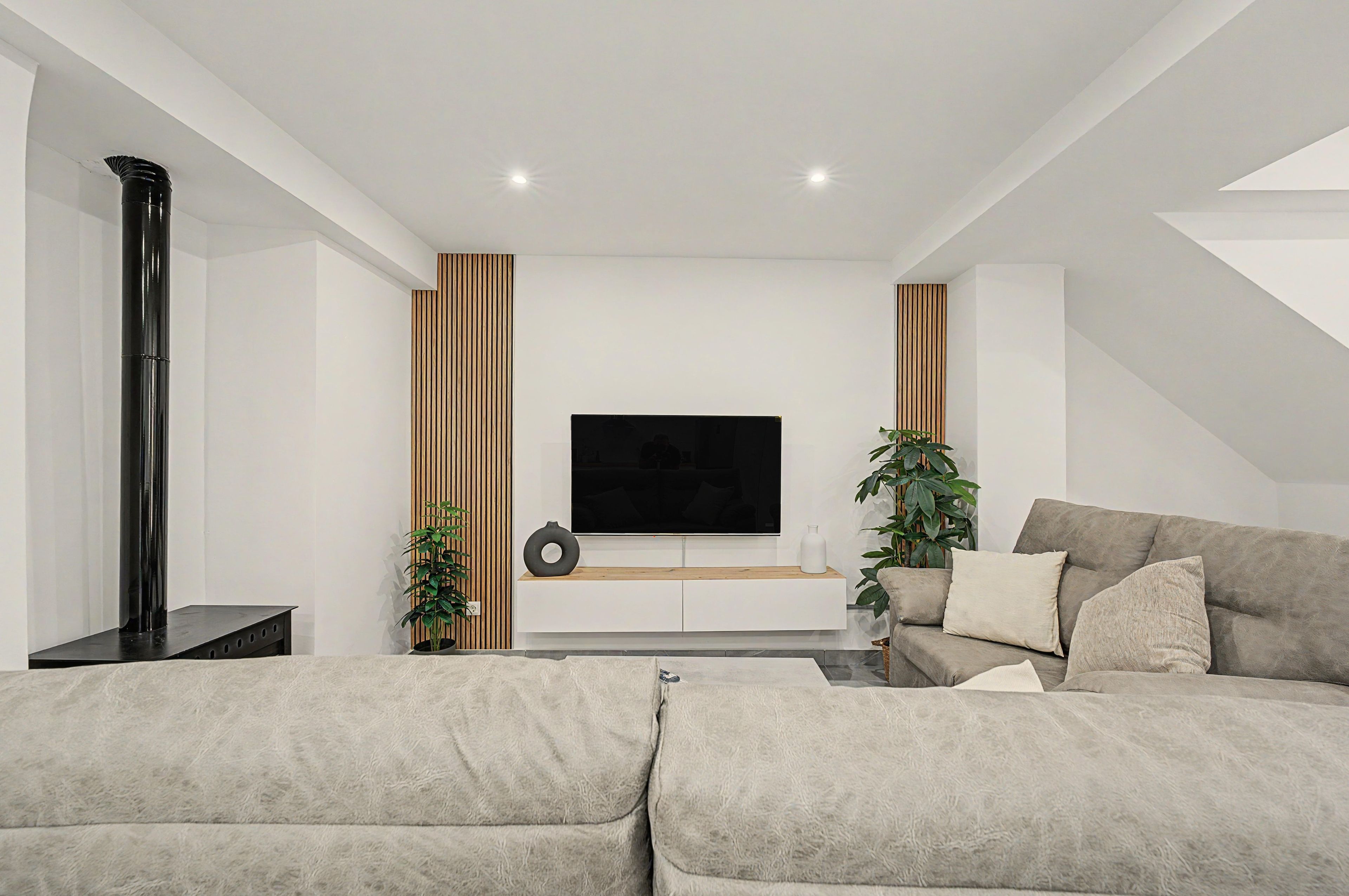 Una sala de estar moderna con un televisor de pantalla plana, un columnario negro alto y un sofá gris.