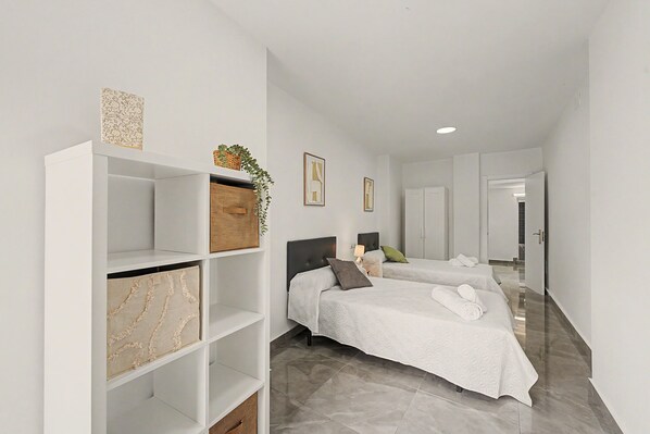 Una habitación de hotel moderna con dos camas, un armario y un amplio estante blanco.