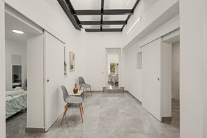 Moderni hotellihuone, jossa on lasikatto, kukallinen päiväpeite sängyllä, pieni pöytä maljakolla ja tuoli.