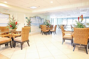 A spacious indoor area with wicker furniture and potted plants, featuring a large window with a view of the ocean. - 4201 Coastal Highway Unit 404 (Ocean City)