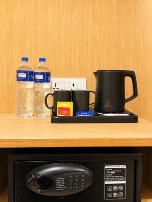 Et minibord på et hotel med vand på flaske, kaffemaskine, sukker og en fjernbetjening.