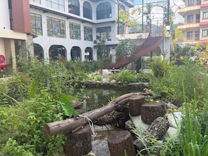 A courtyard with a pond, surrounded by lush greenery and a building with arched windows. - Hotel Lumen - A Garden of Lights (Pokhara)