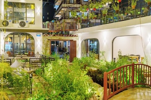 An indoor garden with a wooden bridge, tables, and chairs, surrounded by various plants and greenery. - Hotel Lumen - A Garden of Lights (Pokhara)