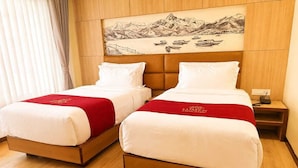 A hotel room with two beds, a wooden headboard, a nightstand, and a painting of a mountainous landscape. - Hotel Lumen - A Garden of Lights (Pokhara)