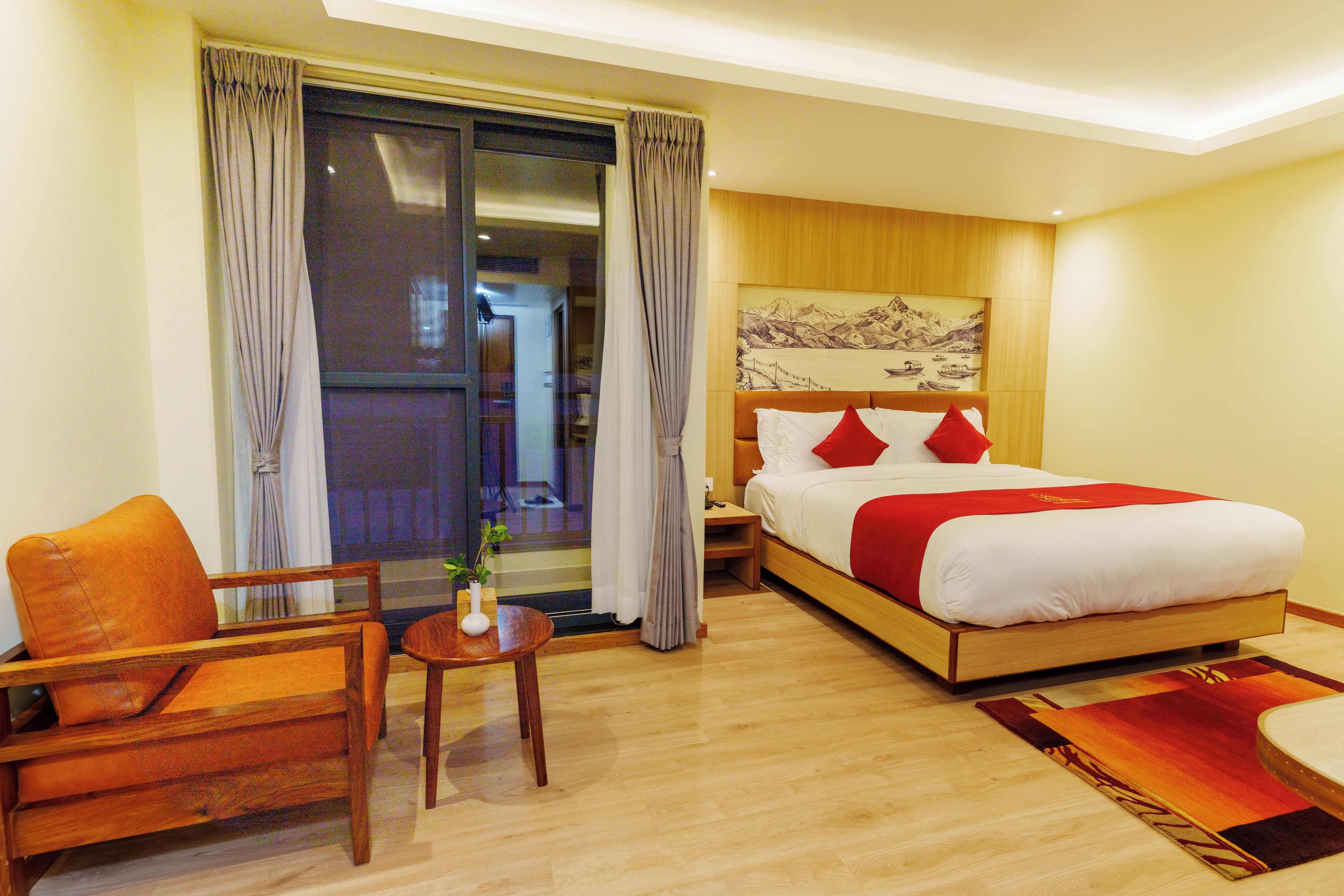 Een hotelkamer met een bed, een stoel, een klein tafeltje met een plant en uitzicht op het omliggende landschap door een schuifdeur.