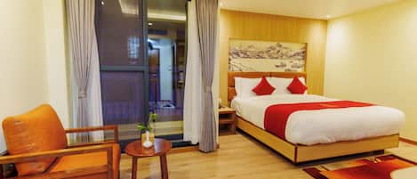 A hotel room with a bed, a chair, a small table with a plant, and a view of the outside through a sliding door.