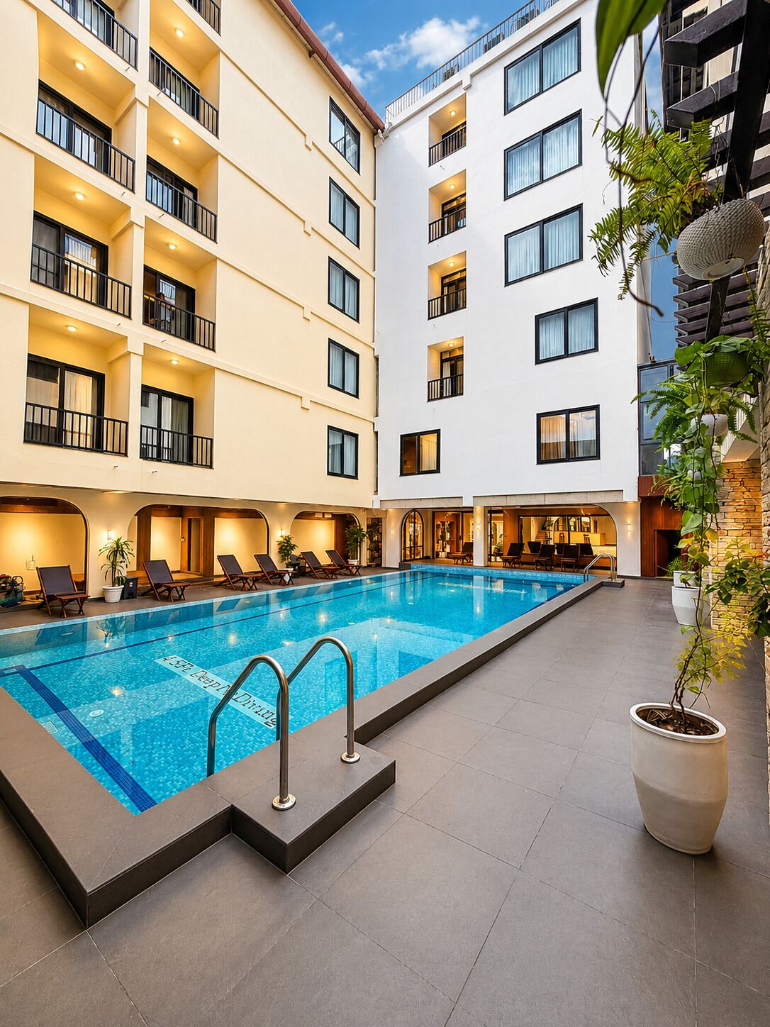 Un espace piscine d’hôtel avec une piscine à l’eau cristalline, des chaises longues et une plante en pot.