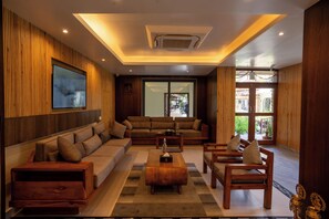 A modern living room with a sectional sofa, a coffee table, and a TV mounted on the wall. - Hotel Lumen - A Garden of Lights (Pokhara)