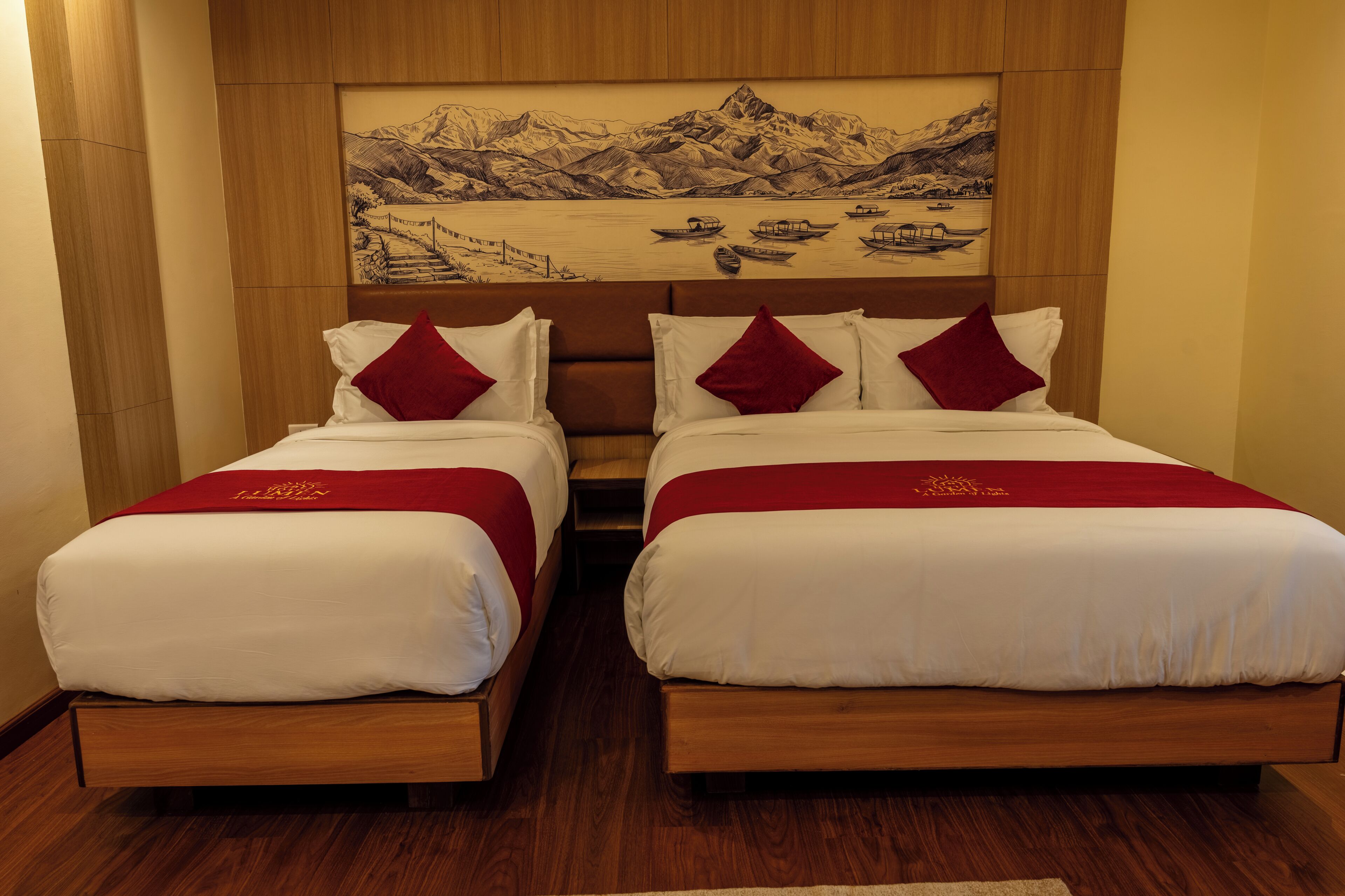 A hotel room with two beds, wooden headboards, and a large landscape painting above.