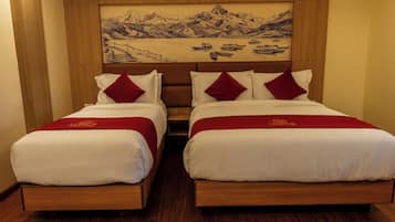 A hotel room with two beds, wooden headboards, and a large landscape painting above.