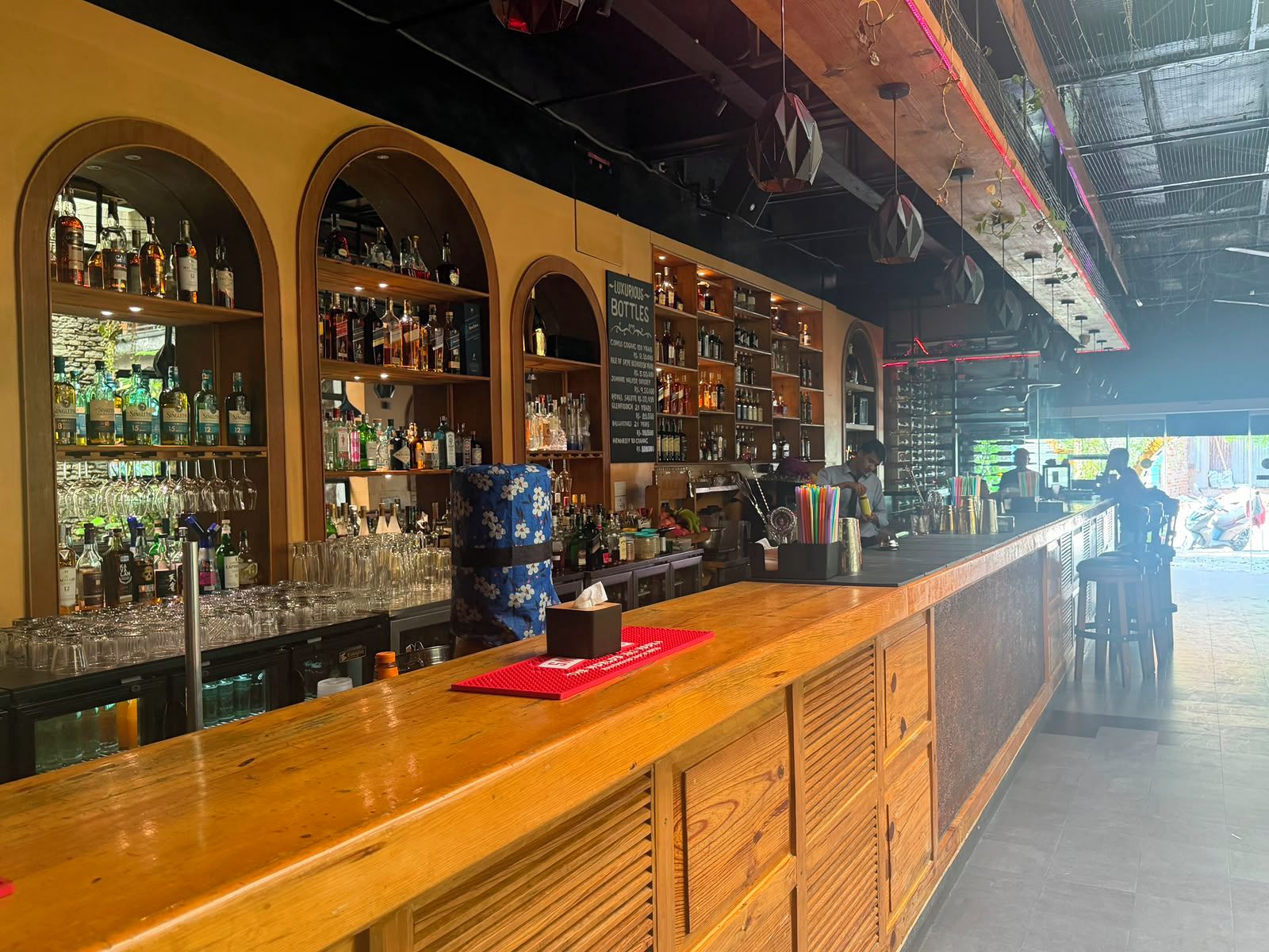 A bar area with shelves of liquor bottles, glasses, and a wooden counter.