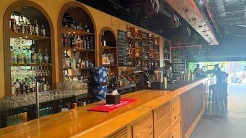 A bar area with shelves of liquor bottles, glasses, and a wooden counter.