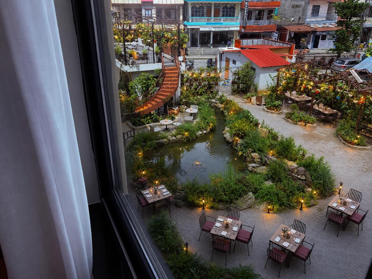 Un patio con un elemento acuático central, rodeado de mesas y sillas, y edificios al fondo.